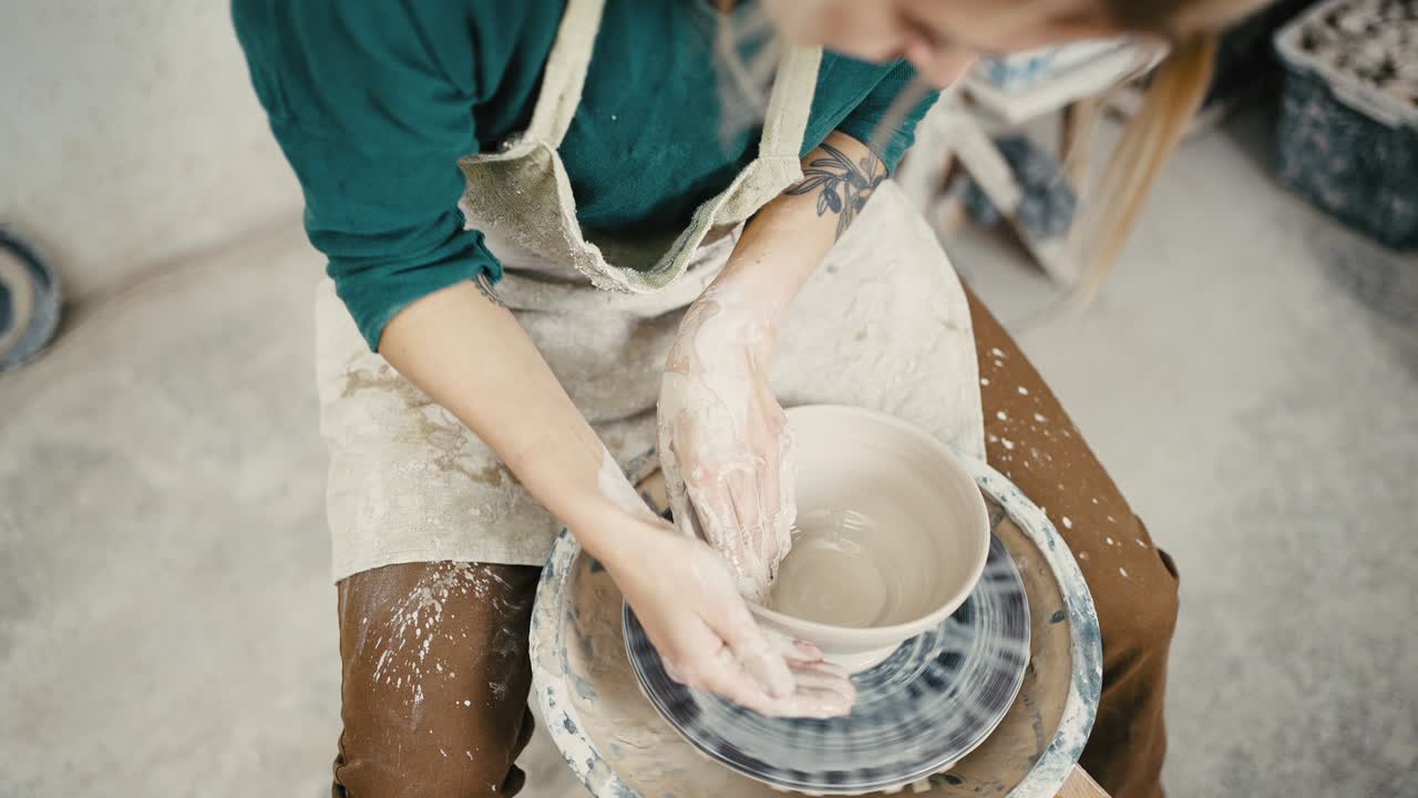 Above view of female potter sculpting ceramic pottery on spinning pottery wheel, using water, tracking shot, slow motion