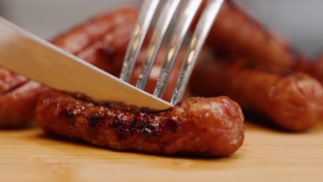 fork stabs cooked breakfast sausage and dull knife tries to cut through on cutting board in slow motion