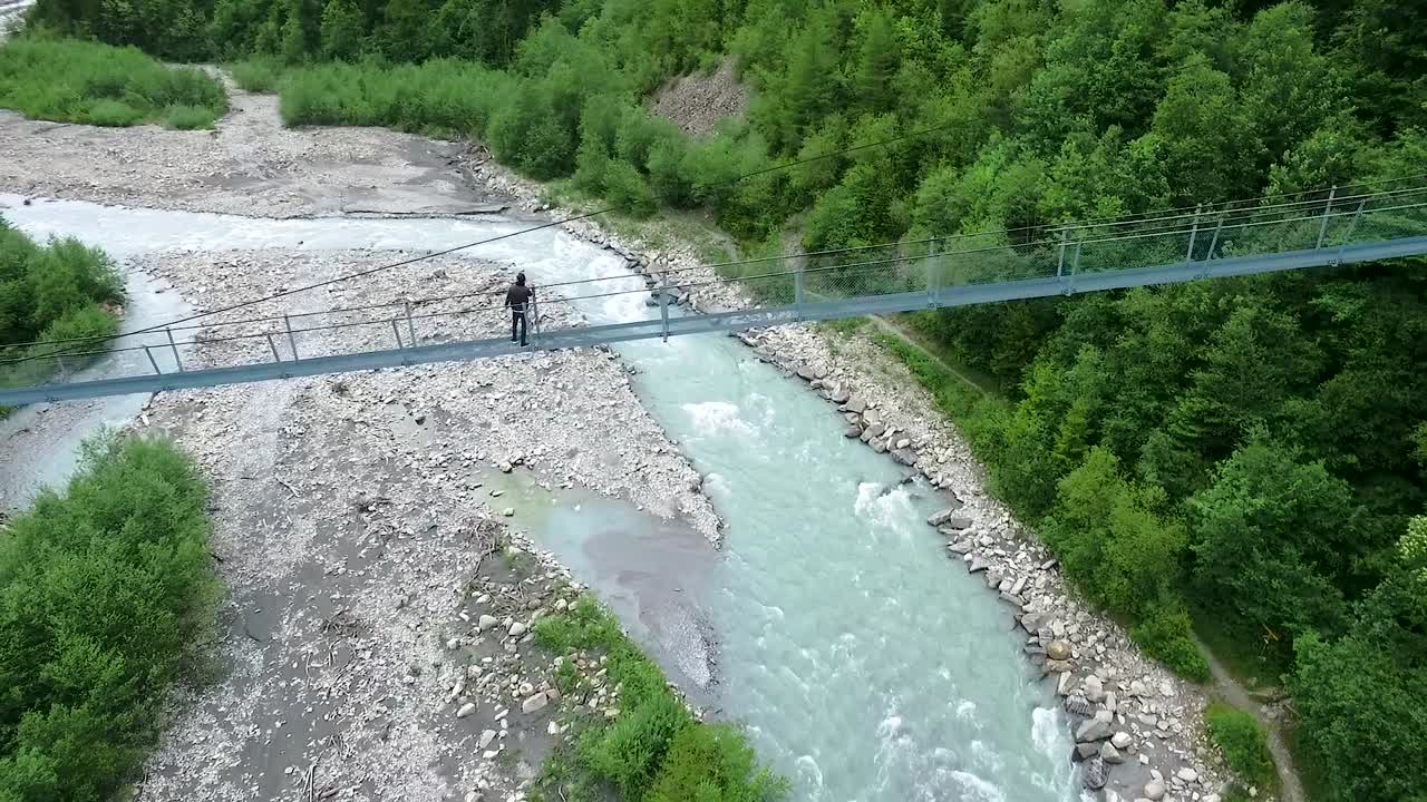 persona en un puente colgante sobre un río de montaña
