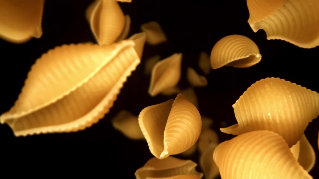Pasta conchiglie dorata che cade al rallentatore su sfondo nero