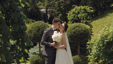 Newlyweds,-caucasian-groom-with-bride-walking,-embracing,-hugs-making-a-kiss-in-park,-wedding-couple