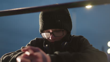 close-up of a young boy wearing glasses and a black jacket, with his head bowed and looking thoughtful, he has a headset around his neck, and his hands are clasped in front of him