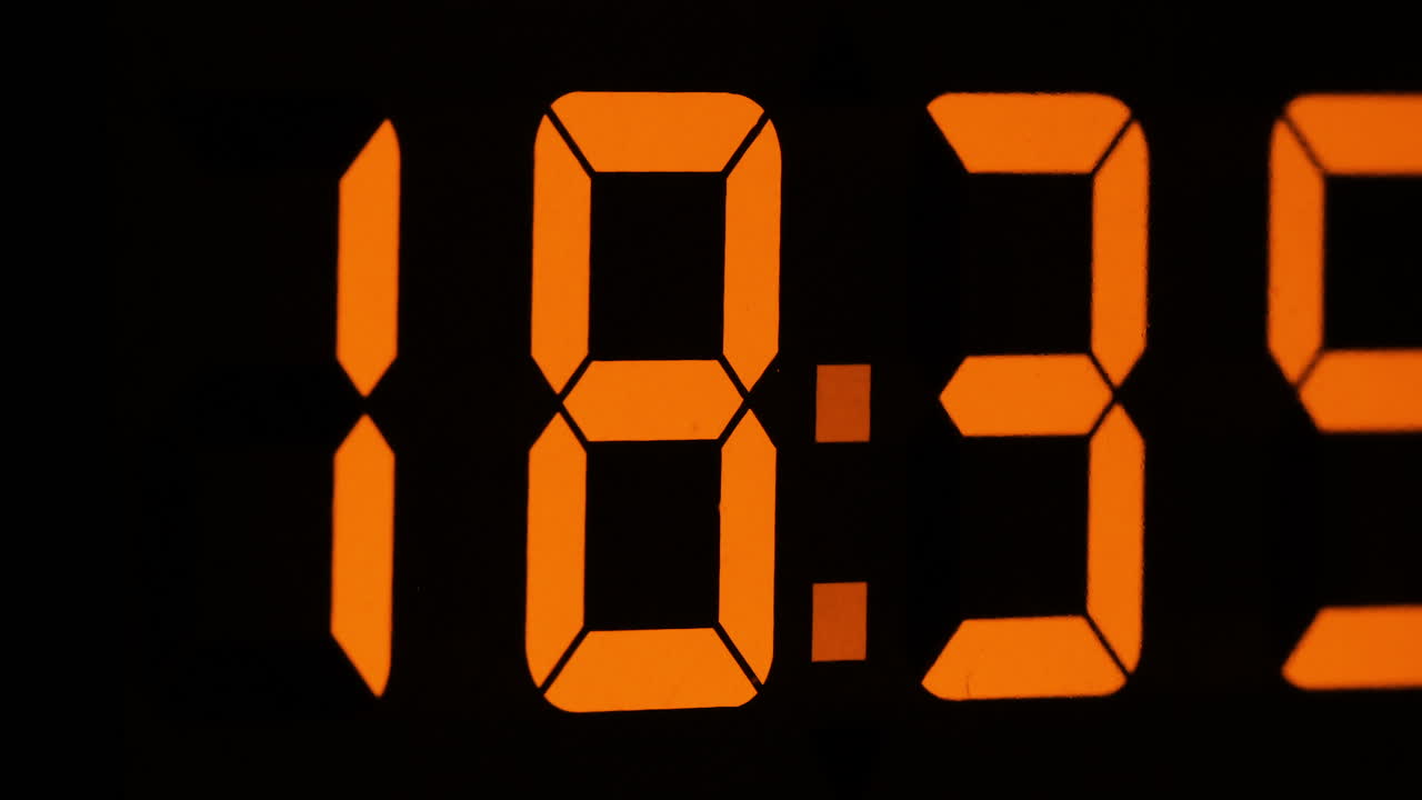 Timelapse zoom in shot of orange display digital clock with hours flying by