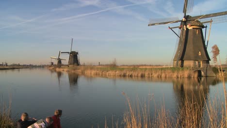 Los-Niños-Juegan-Frente-A-Los-Molinos-De-Viento-A-Lo-Largo-De-Un-Canal-En-Holanda