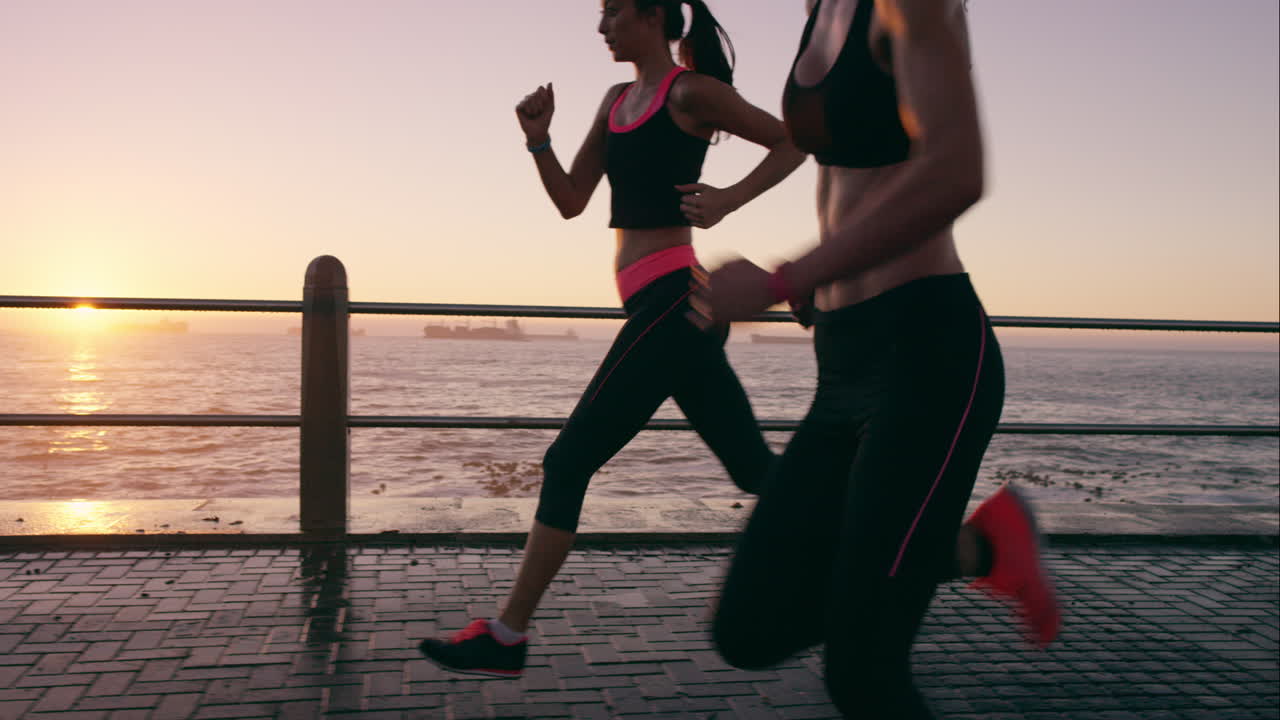 dos mujeres atléticas corriendo al aire libre en cámara lenta en el paseo marítimo al atardecer cerca del océano disfrutando de la carrera nocturna