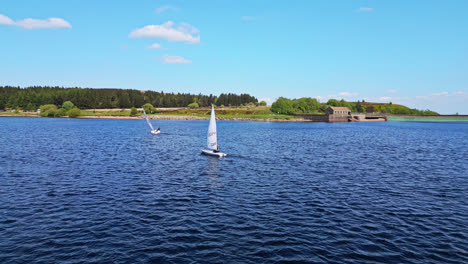 amidst the picturesque beauty of winscar reservoir in yorkshire, sailing club members embark on a thrilling boat race, their white sails standing out against the serene blue lake