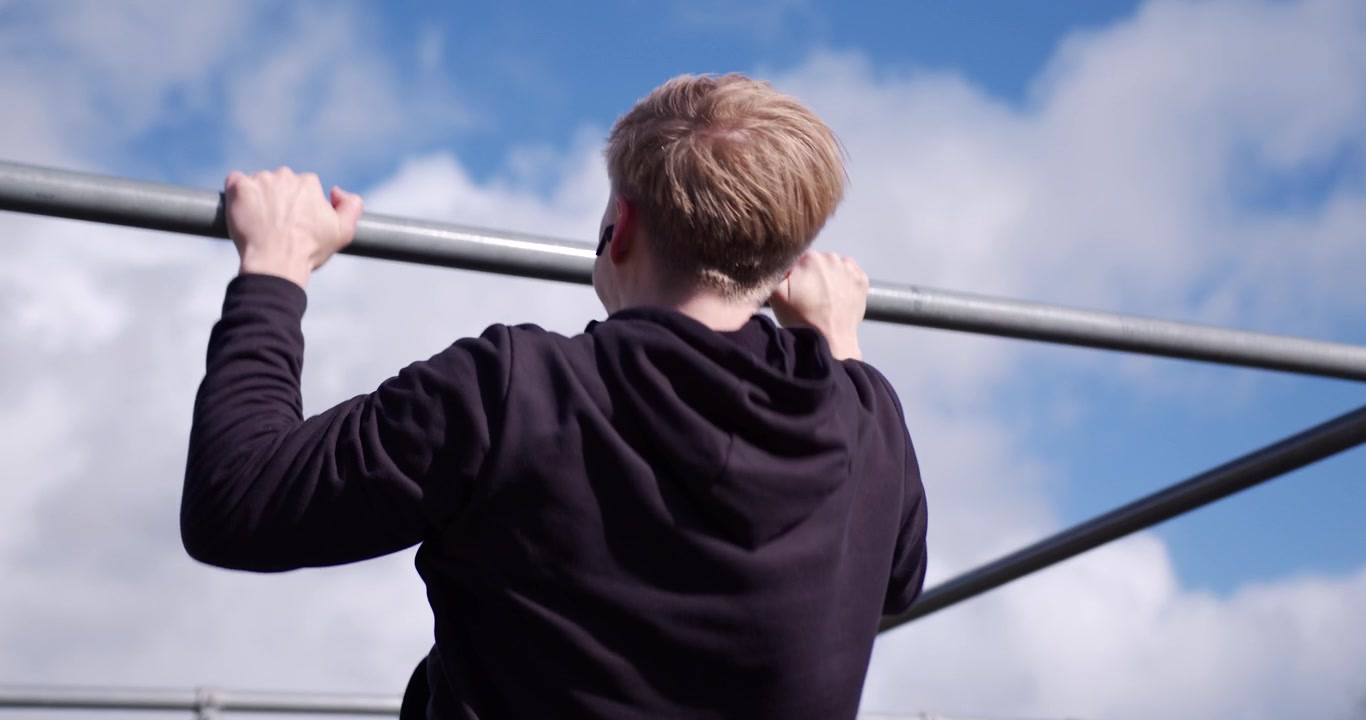 Young fit male athlete doing a pull up exercise on a bar in the outdoor gym