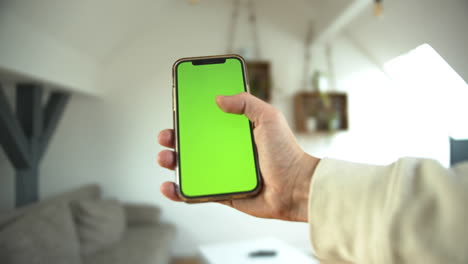 un hombre sosteniendo un teléfono inteligente con pantalla verde tocando el móvil en el fondo blanco de una casa