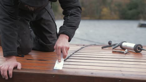 carpenter repairing cabin roof of boat sealing leaks flattening mastic waterproof sealant