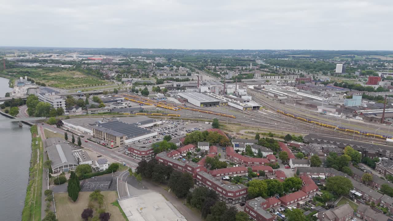 Filmato aereo con drone del vasto scalo ferroviario vicino alla stazione di Maastricht, inclusi binari, treni, zone industriali e aree residenziali adiacenti lungo il fiume Maas.