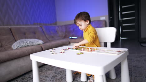 two-year-old toddler playing with wooden puzzles sitting at desk. baby boy combining game and studying.