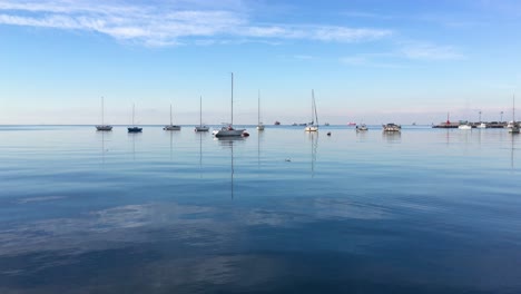 Calm-blue-sea-with-sky-reflection-and-small-boats
