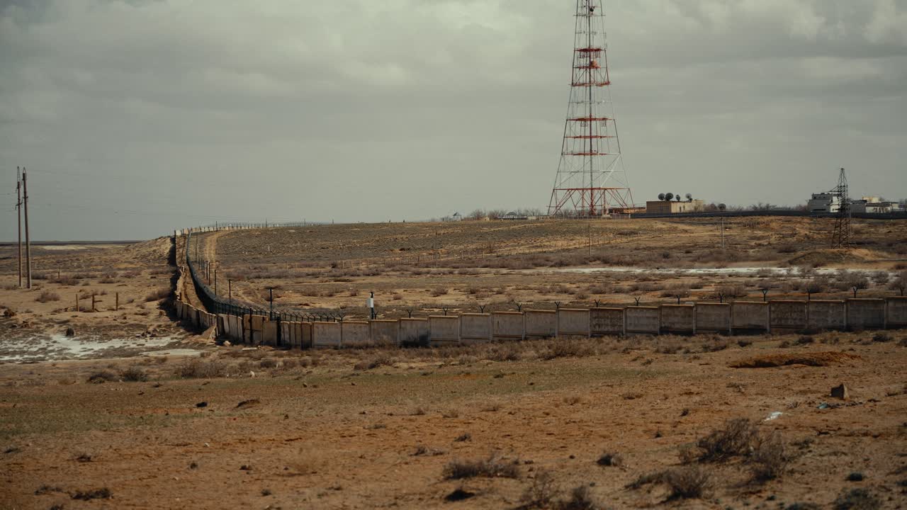 Persona caminando a lo largo de una valla larga en un paisaje desértico desolado.