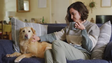 Una-Mujer-Caucásica-Sonriente-Acariciando-A-Su-Perro-Sentado-En-Un-Sofá-En-Casa