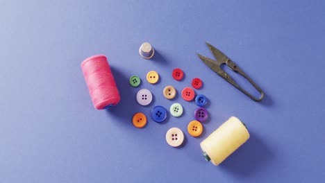 video of thread snippers, thimble, buttons and reels of cotton on blue background