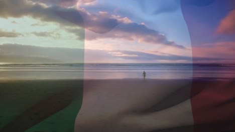 이탈리아 국기 의 디지털 구성 은 해변 에서 서핑 보드 를 들고  ⁇ 고 있는 사람 에 대항 하여 흔들리고 있다