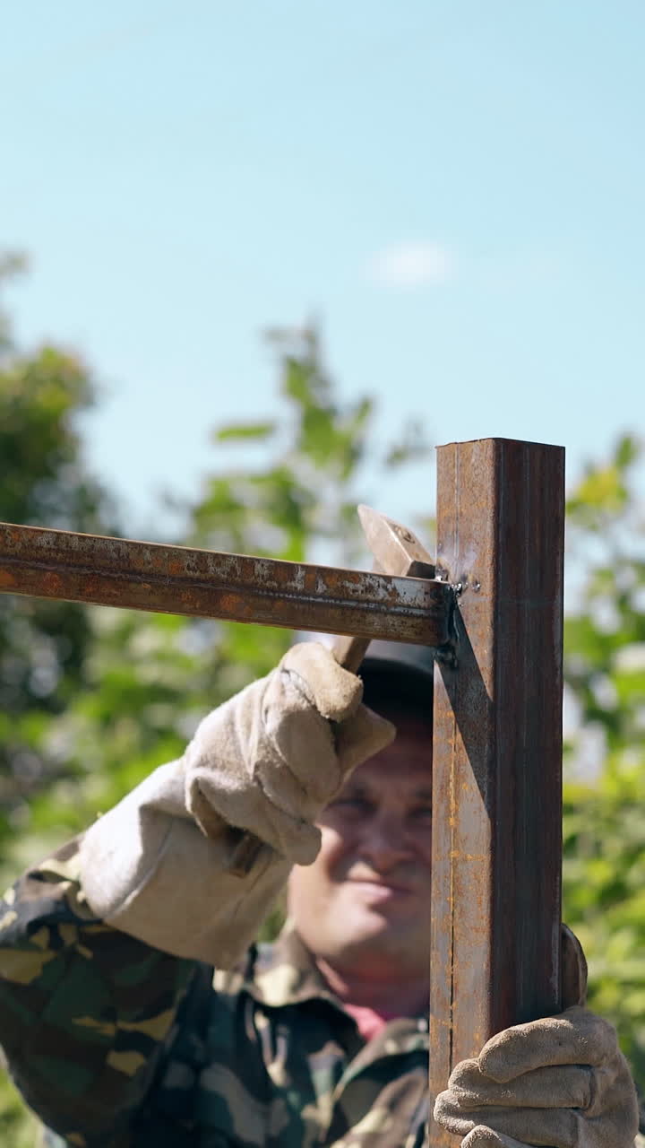professional builder in open welding mask checks quality of fence tapping with hammer and jumping up on carcass