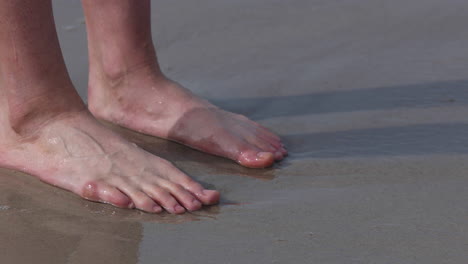 ondas do mar espirrando sobre os pés femininos em pé descalço na costa do mar, close-up