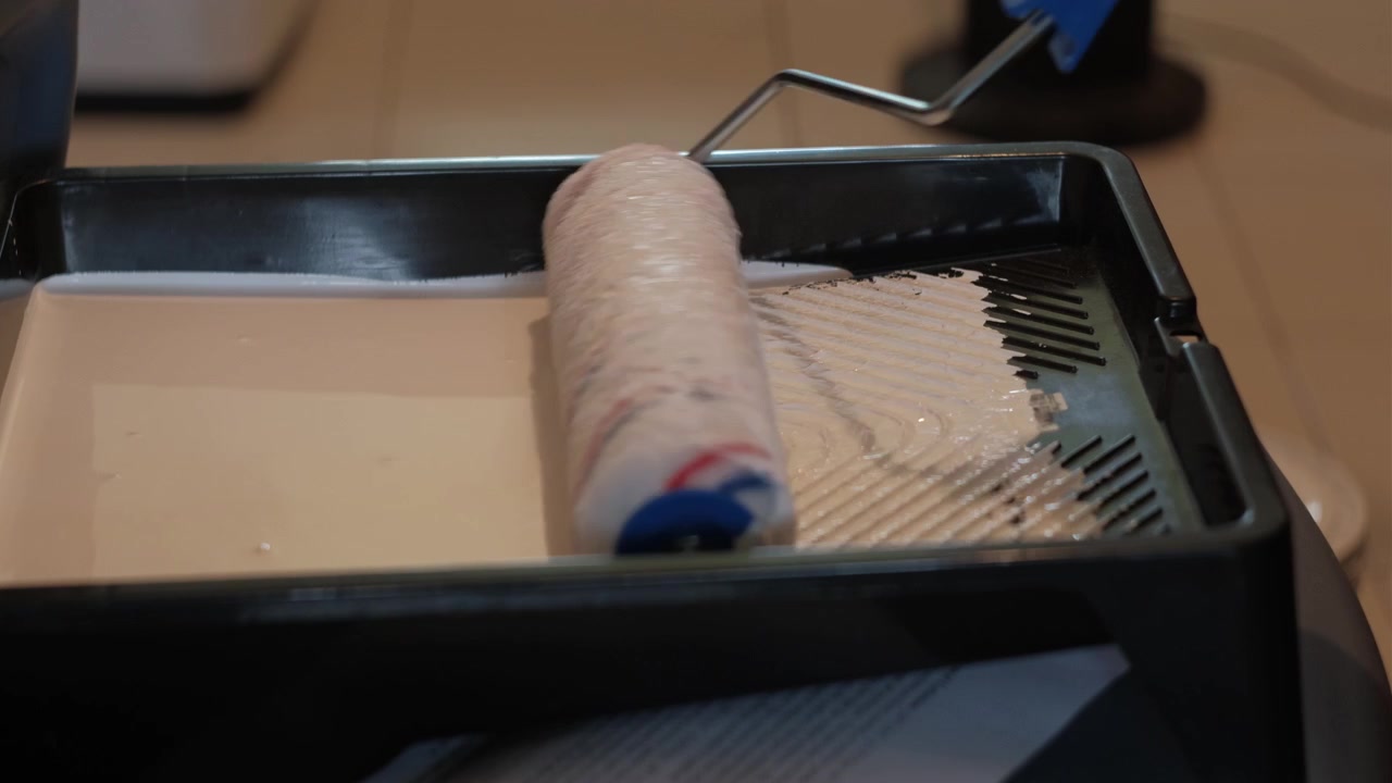 Primo piano di un rullo per pittura che assorbe vernice bianca da un vassoio durante lavori di pittura e ristrutturazione interni.