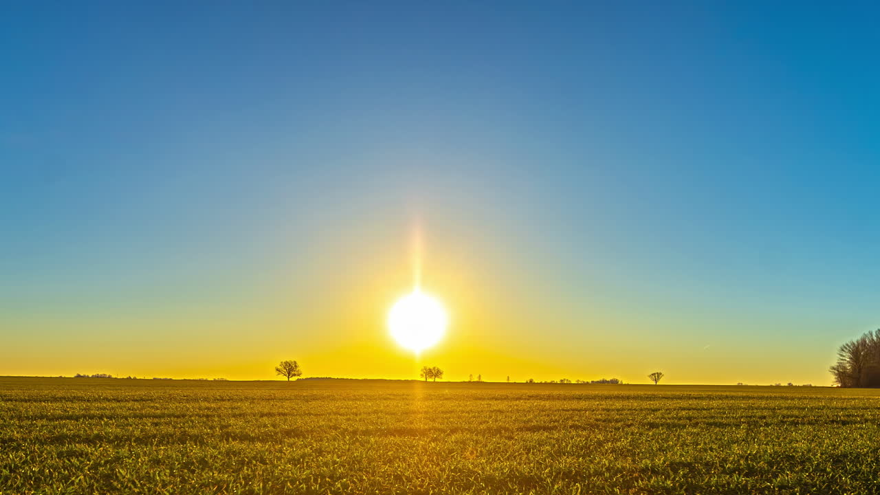 Timelapse af solopgang over åbent landbrugsland, mens solen når en flad horisont og fylder himlen med en orange til blå gradient – ren, minimal baggrund til titler og reklamer