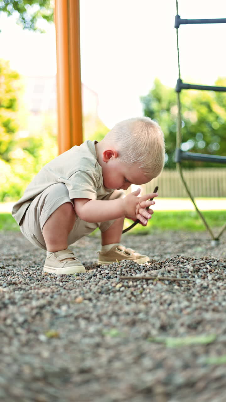 Bambino biondo di 2 anni in pantaloncini e maglietta che gioca al parco giochi. Bambino piccolo a passeggio all'aria aperta. Il bambino gioca autonomamente in strada. Autosviluppo del bambino