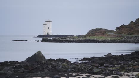 Statische-Meereslandschaft,-Schwarze-Felsen-Im-Vordergrund,-Langer-Leuchtturmfelsen,-Insel