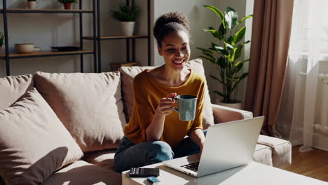happy woman working or relaxing at home on couch with laptop and mug