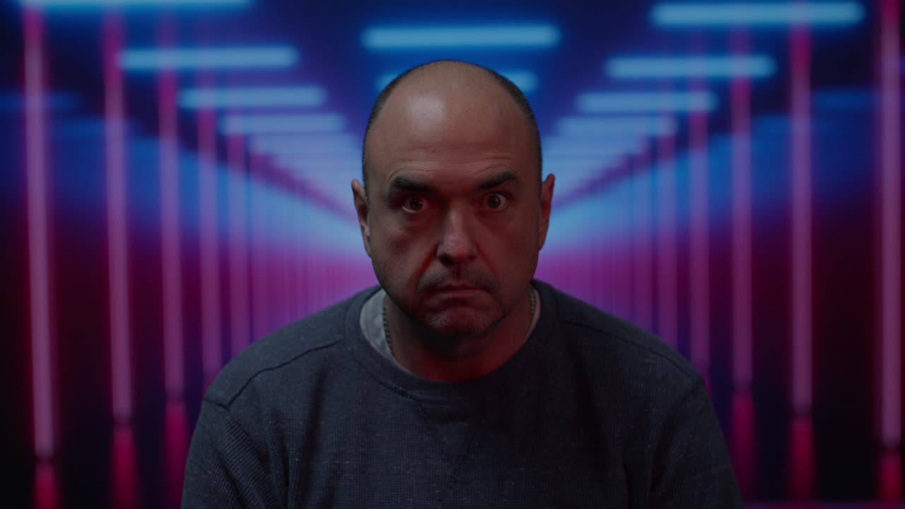 hombre blanco de mediana edad mirando a la cámara con una mirada en blanco con un fondo colorido en movimiento