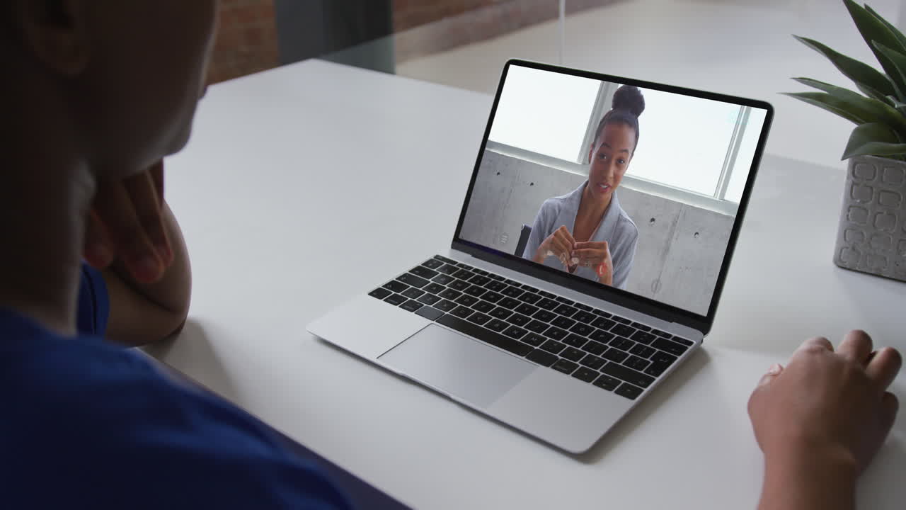 Mulher negra conversando em uma chamada de vídeo no notebook com uma colega de trabalho em casa.