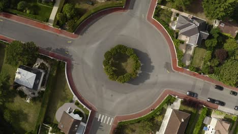 top drone aerial view of traffic roundabout, traffic circle with green trees orange sidewalks and green grass above french typical houses in deauville, france. black car passing by 4k uhd.