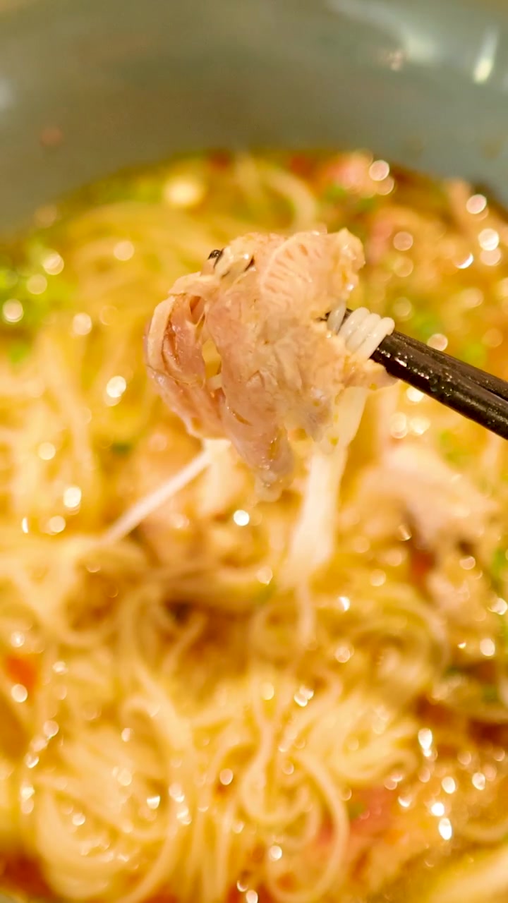 Le bacchette sollevano noodles e carne da una vivace zuppa vietnamita, mettendo in mostra colori e consistenze ricchi in un ambiente caldo.