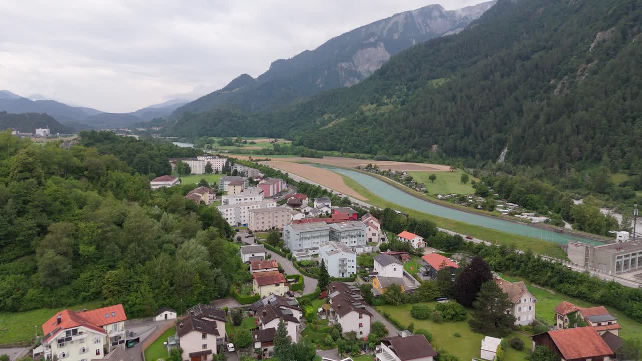 Aerial wide shot of Swiss village with river and green alp mountains in Switzerland. Cloudy summer day in domat Ems