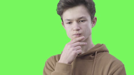 close-up of thoughtful brunette boy with brown eyes. portrait of philosophical caucasian teenager thinking and rubbing face at green background. contemplation, planning, lifestyle. chromakey.