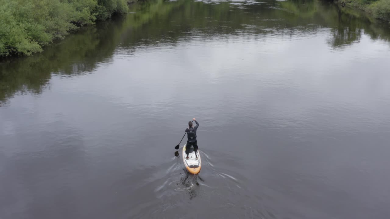 antena sigue stand up paddleboarder remando en un pequeño río rural