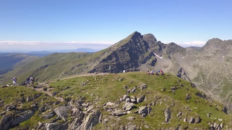 drone orbiting high mountain peak with hikers resting after ascent to the summit