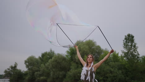una joven artista muestra trucos de magia usando enormes burbujas de jabón. crear burbujas de jabón usando palos y cuerda al atardecer para mostrar un espectáculo de circo teatral