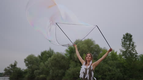 a young girl artist shows magic tricks using huge soap bubbles. create soap bubbles using sticks and rope at sunset to show a theatrical circus show