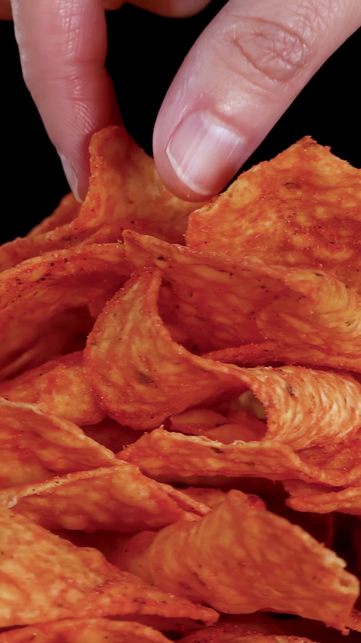 Chips de nacho dourados giram sob iluminação de estúdio, destacando a textura e a crocância com um close-up dramático.