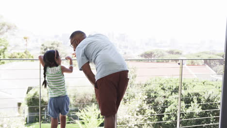 Biracial-grandfather-and-biracial-granddaughter-enjoy-a-view-from-a-balcony-with-copy-space