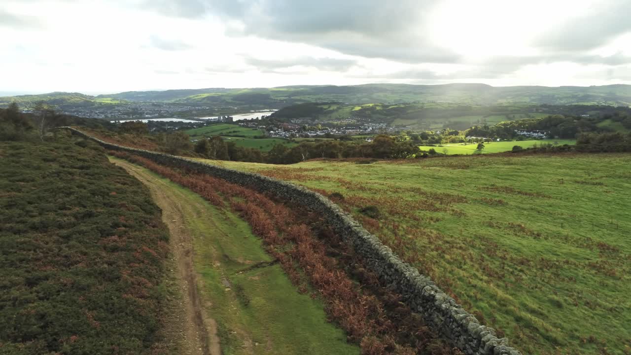Sunbeams moving across overcast British agricultural rural village countryside morning aerial low dolly left view