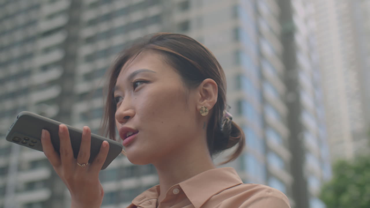 Asian Businesswoman Talking on Speakerphone on Urban Street