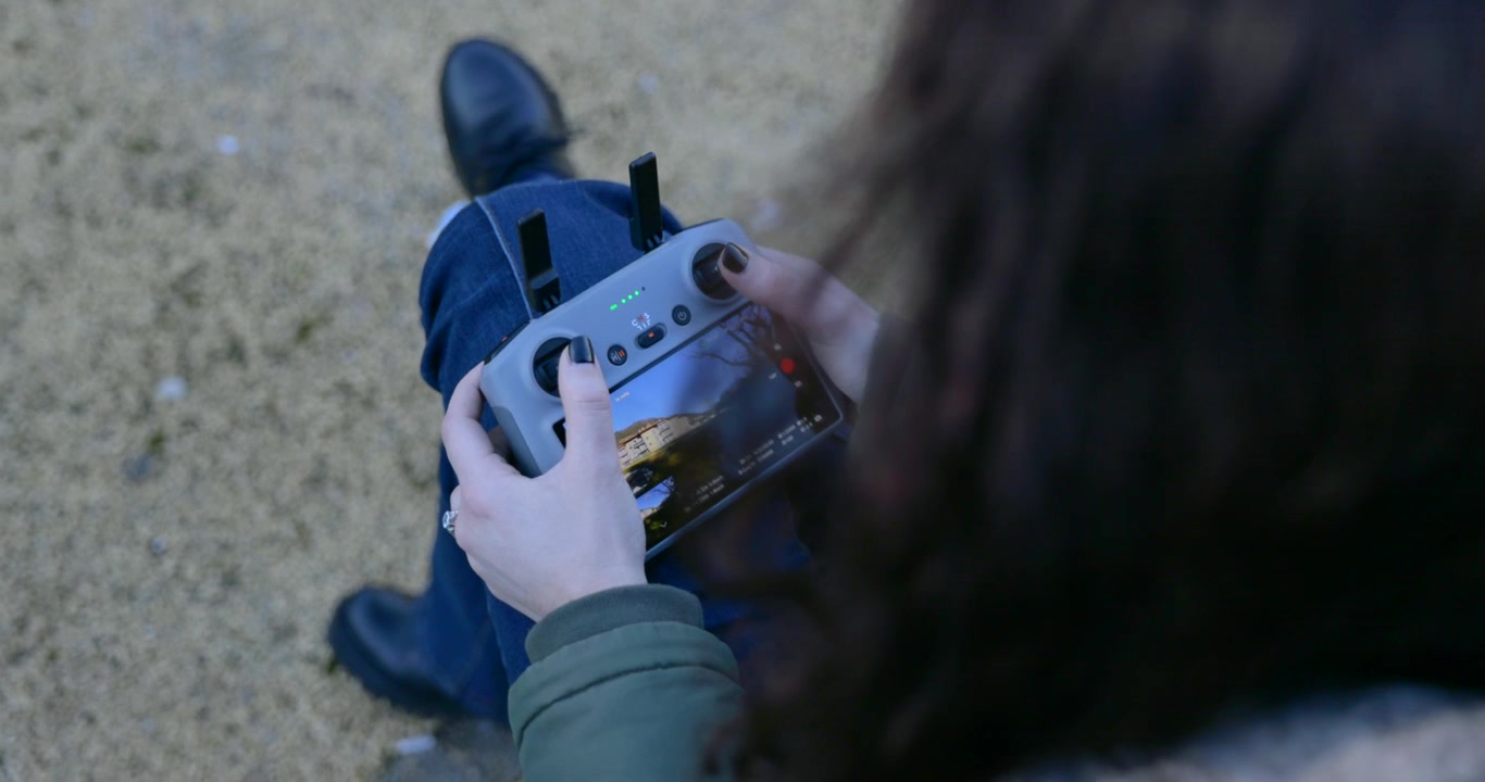 Donna seduta su una panchina che aziona un telecomando per drone con schermo display all'aperto