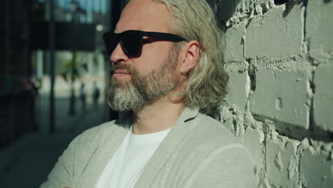 man with sunglasses leaning against a brick wall