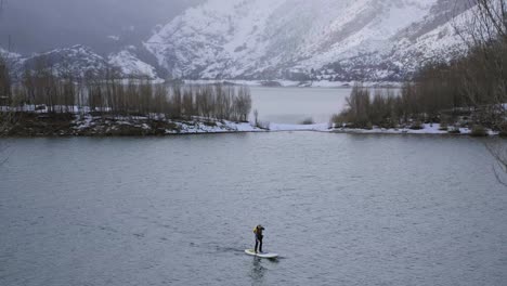 man on paddle board between water and mountains on coast