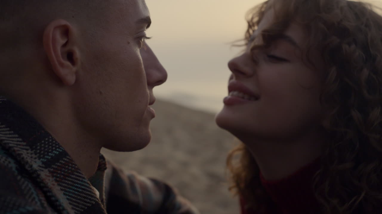 Coppia innamorata che si bacia sulla spiaggia oceanica al tramonto. Donna sorridente che guarda l'uomo.