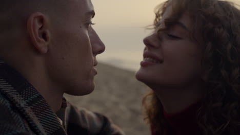 loving couple kissing on ocean beach at sunset. smiling woman looking on man