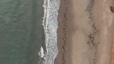 top view of waves splashing on the sandy shore at the beach in magdalen islands, quebec, canada - aerial drone