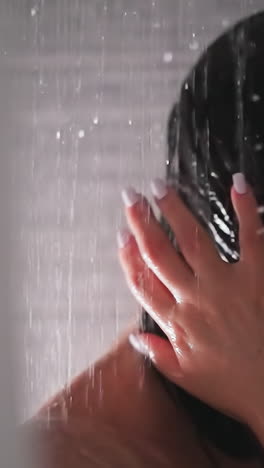 woman washes away shampoo from hair shower unit. brunette lady strokes short hair under falling down water drops in bathroom. regular procedure