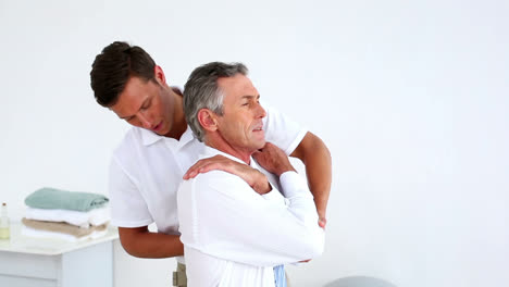 Stressed-businessman-getting-his-shoulders-aligned-by-physiotherapist-