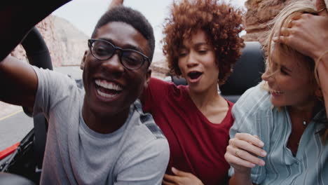 group of young friends in back of open top hire car on summer vacation